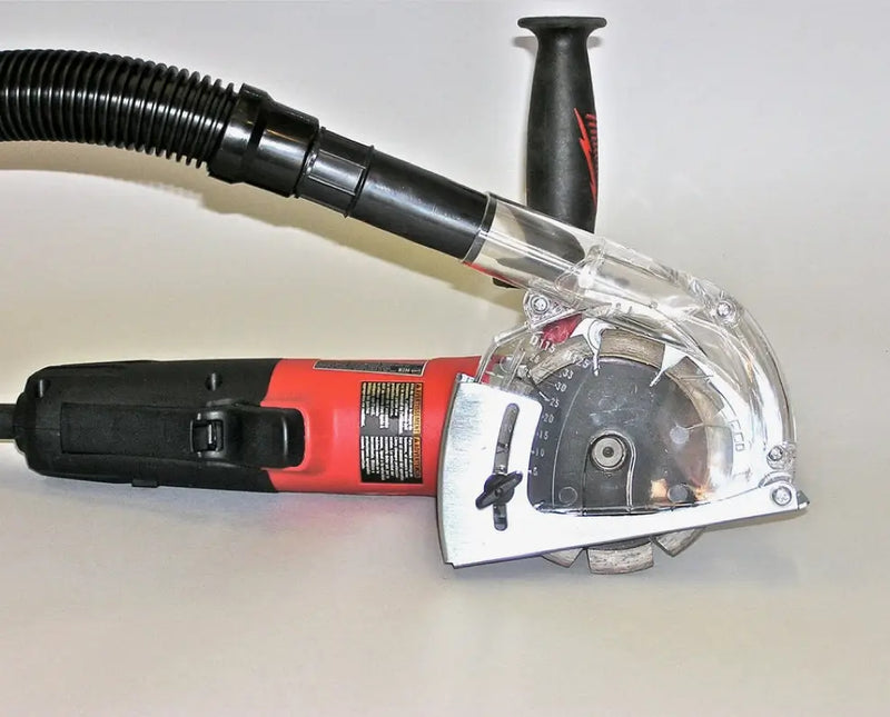 Red and black angle grinder equipped with a clear transparent dust shroud attachment and black hose for dust extraction resting on a white background, clearly showing details of the protective attachment and blade.

